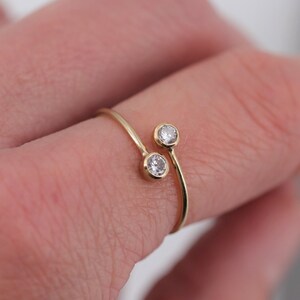 Könnte beinhalten: Ein goldener Ring mit zwei kleinen, klaren Edelsteinen. Der Ring ist so konzipiert, dass er sich um den Finger wickelt.