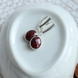 Könnte beinhalten: Ein Paar silberne Ohrringe mit roten Edelstein-Tropfen. Die Ohrringe haben ein schlichtes Design und sind perfekt für den Alltag.