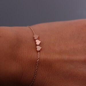 May include: A delicate rose gold chain bracelet with three small heart charms.