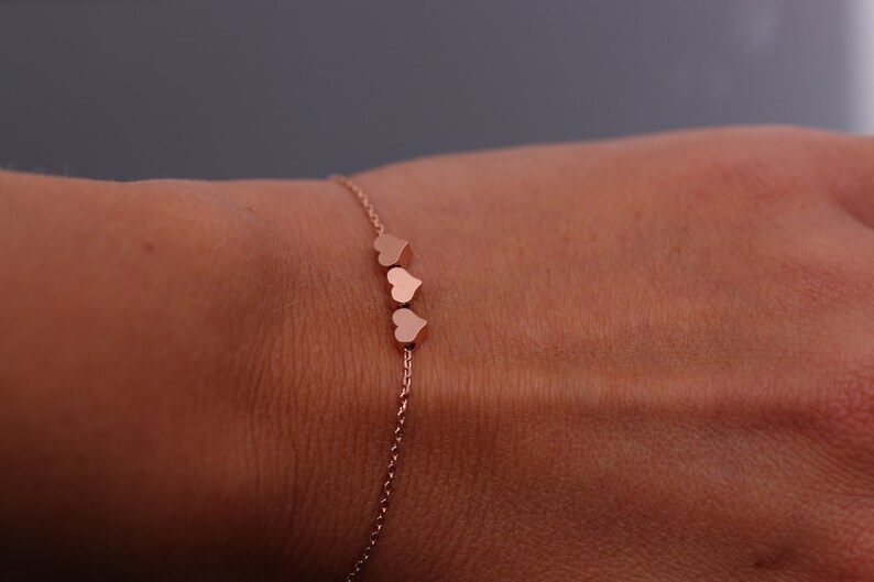 May include: A delicate rose gold chain bracelet with three small heart charms.