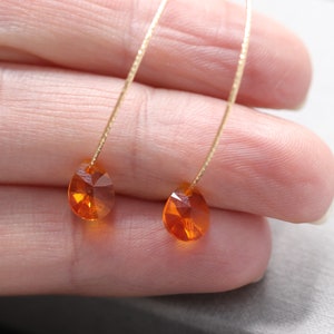 Könnte beinhalten: Ein Paar zarte goldene Ohrringe mit kleinen, tropfenförmigen orangefarbenen Edelsteinen.