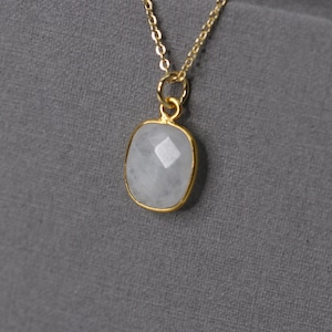 Könnte beinhalten: Eine goldene Kettenkette mit einem weißen Edelstein-Anhänger. Der Anhänger ist rechteckig mit einem facettierten Design.