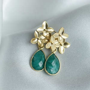 Può includere: Orecchini in oro con un gruppo di piccoli ciondoli a forma di fiore e pietre preziose verdi a forma di lacrima.