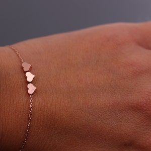 May include: A delicate rose gold bracelet with a chain and three small heart charms.