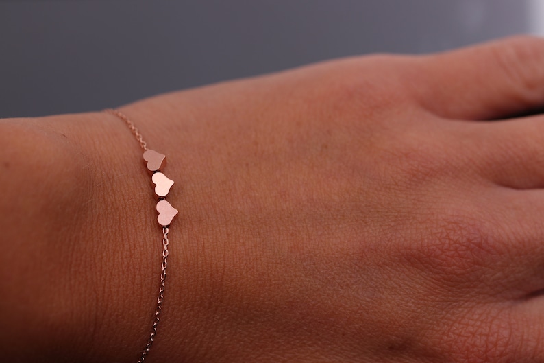 May include: A delicate rose gold bracelet with a chain and three small heart charms.