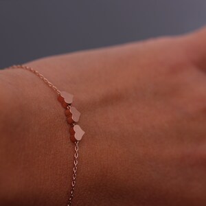 May include: A delicate rose gold bracelet with a chain and three small heart charms.