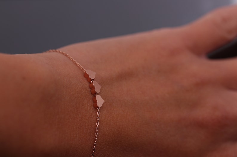 May include: A delicate rose gold bracelet with a chain and three small heart charms.