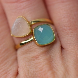 May include: A gold ring with two gemstones. The larger gemstone is a square, light blue color. The smaller gemstone is a triangular, light pink color.