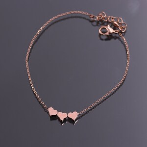 May include: A delicate rose gold chain bracelet with three small heart charms.