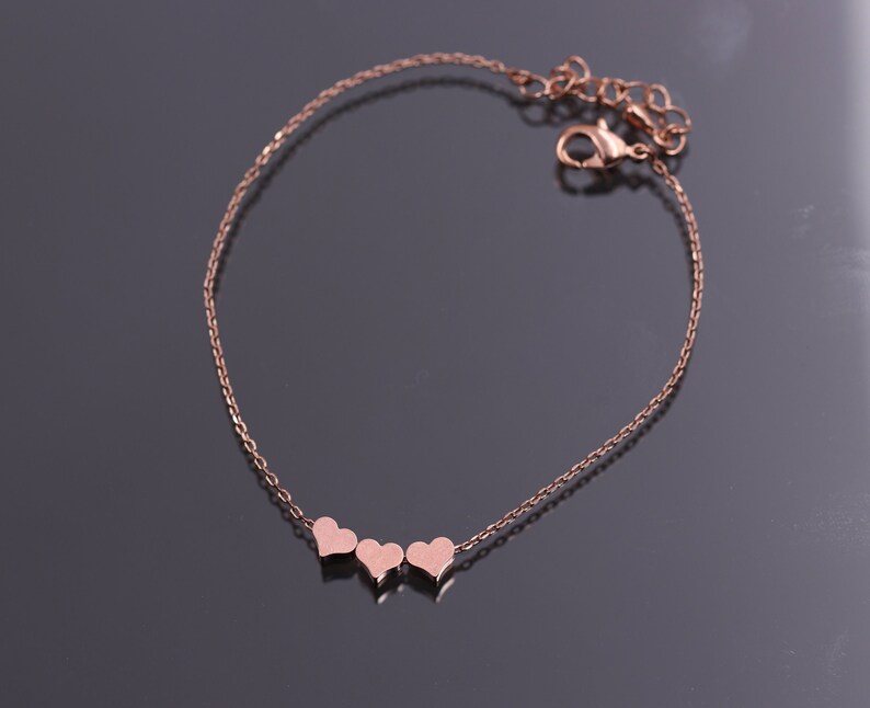 May include: A delicate rose gold chain bracelet with three small heart charms.