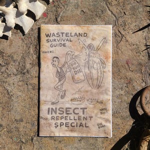 May include: A weathered booklet titled "Wasteland Survival Guide" with Issue #2 displayed. The cover features a cartoon illustration of a person spraying insect repellent at a creature. The text "Insect Repellent Special" is also visible.