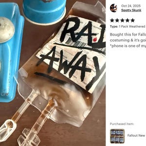 May include: A clear plastic IV bag filled with a brownish liquid, featuring the text RAD AWAY written in bold black letters on a white label. The bag includes attached clear plastic tubing with a white plastic clamp and a blue rotary telephone.