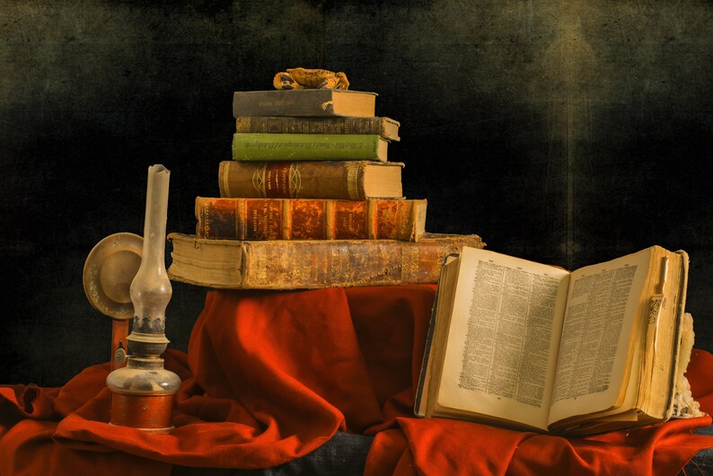 A stack of antique books with leather covers and a worn open book on a red cloth surface. An oil lamp with a glass chimney sits on the left side of the image. These books represent the ebooks that are included in this downloadable pack of rare witchcraft, magical, spell craft, and paganism books.
