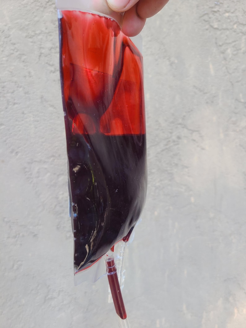 May include: A transparent plastic bag containing a dark red liquid, similar to blood. A tube is connected at the base. The liquid is a deep, rich red, with a slightly lighter hue at the top.