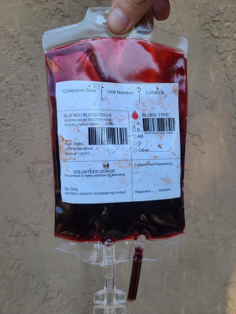 May include: A transparent plastic bag filled with a dark red liquid, resembling blood. The bag has a label with text including "SL-5 RED BLOOD CELLS" and "VOLUNTEER DONOR". The bag has a clear tube and a white label with text.