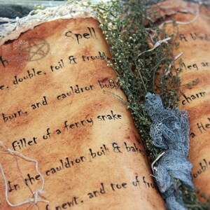 A close-up of a vintage book with a brown leather cover and a handwritten inscription that reads "Witch Spell Double, double, toil & trouble Fire burn, and cauldron bubble Fillet of a fenny snake In the cauldron boil & bake newt, and toe of frog Double, double, toil and trouble Fire burn and cauldron bubble Fillet of a fenny snake In the cauldron boil and bake newt, and toe of frog". This represents the ebooks that are included in this downloadable pack of rare witchcraft.