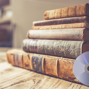 May include: A stack of vintage, leather-bound books with a silver CD on a wooden table.