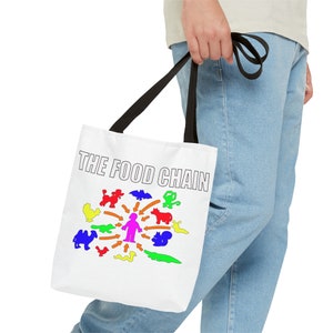 May include: White tote bag with black handles and the text "THE FOOD CHAIN" printed in black. The bag features a colorful illustration of a person surrounded by various animals, including a chicken, a poodle, a bat, a monkey, a cow, a squirrel, a camel, a crocodile, and a worm.