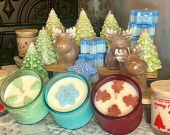 May include: Assortment of Christmas themed candles in various shapes and colors.  Candles include a snowflake, a Christmas tree, and a gingerbread man.  The candles are displayed on a wooden surface.