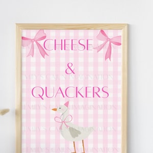 Puede incluir: Impresión enmarcada con un fondo de cuadros rosas y las palabras "CHEESE & QUACKERS" en rosa. Un dibujo de un ganso con un gorro de fiesta y un lazo está en la parte inferior. Dos lazos rosas están en la parte superior.