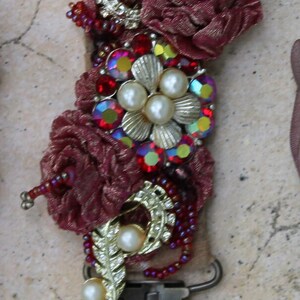 May include: A burgundy fabric flower embellishment with gold and pearl accents, red and iridescent rhinestones, and a metal clasp. The embellishment is labeled with the number "#6".