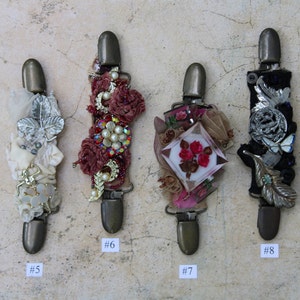 May include: Four decorative fabric-covered clips with embellishments, including beads, sequins, and flowers. The clips are numbered 5, 6, 7, and 8.