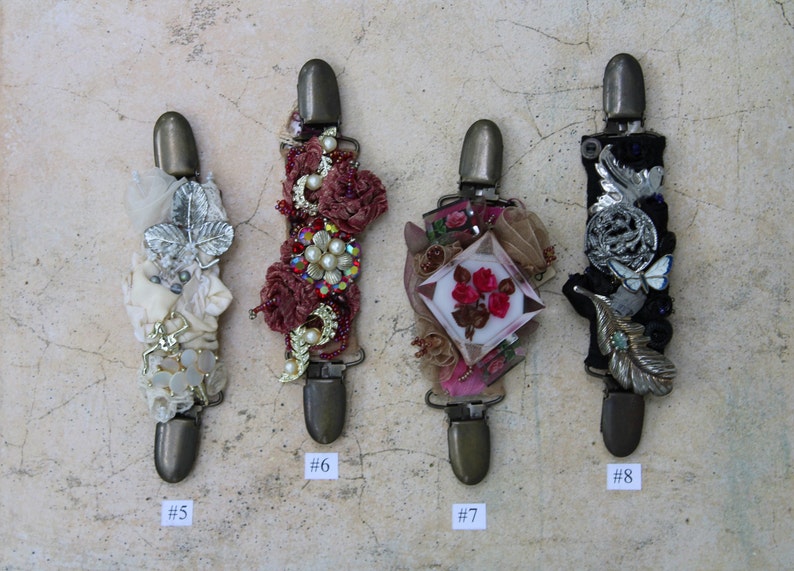 May include: Four decorative fabric-covered clips with embellishments, including beads, sequins, and flowers. The clips are numbered 5, 6, 7, and 8.