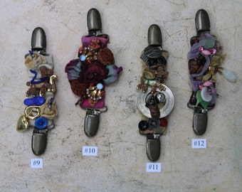 May include: Four decorative metal clips with fabric and embellishments. The clips are numbered 9, 10, 11, and 12.