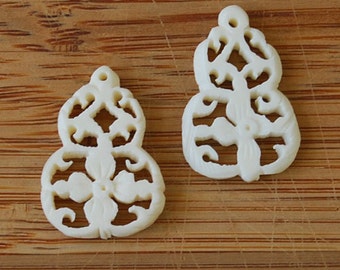 May include: Two white, intricately carved, gourd-shaped pendants with a floral design.