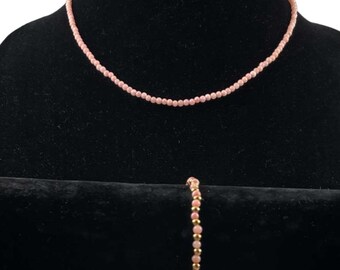 May include: A set of pink bead jewelry, including a necklace and a bracelet. The necklace is longer and the bracelet is shorter. Both pieces are made of small, round beads.