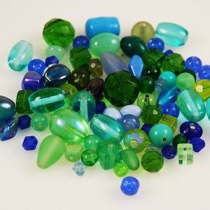 Puede incluir: Una colección de cuentas de vidrio verde, azul y turquesa de varias formas y tamaños. Las cuentas son perfectas para hacer joyas o manualidades.