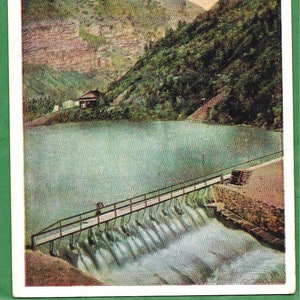 May include: A vintage postcard showing a dam with a wooden bridge and cascading water. The dam is situated in a canyon with lush green trees and a blue sky. The postcard is titled "5548. Power Dam, Ogden Canyon, Utah."