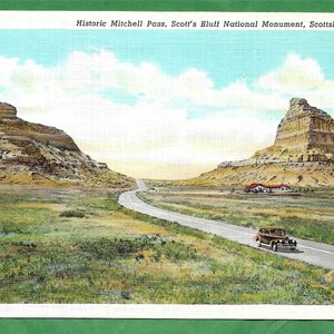Könnte beinhalten: Eine Vintage-Postkarte mit einer malerischen Aussicht auf den Mitchell Pass im Scott's Bluff National Monument in Nebraska. Die Postkarte zeigt eine Straße, die sich durch ein Tal schlängelt, mit zwei großen Felsformationen auf beiden Seiten. Der Himmel ist blau mit weißen Wolken.