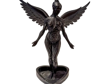 May include: A black anatomical sculpture of a winged figure standing on a heart-shaped base. The figure displays exposed musculature and skeletal structure, with arms extended outward and large, detailed wings spread wide behind the torso.