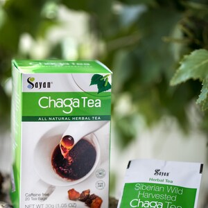 May include: A box of Sayan Chaga Tea with a green background and a cup of tea with a spoon pouring in. The box says "All Natural Herbal Tea" and "Caffeine Free, 20 Tea Bags, Net Wt 30g (1.05 oz)". There is a single tea bag packet in the foreground that says "Sayan Herbal Tea, Siberian Wild Harvested Chaga Tea, All Natural Exclusive Caffeine Free Blend, Net Wt 1.5g".