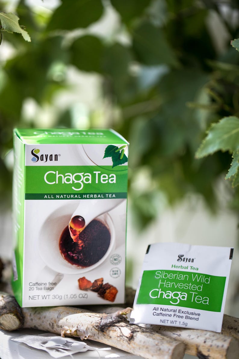 May include: A box of Sayan Chaga Tea with a green background and a cup of tea with a spoon pouring in. The box says "All Natural Herbal Tea" and "Caffeine Free, 20 Tea Bags, Net Wt 30g (1.05 oz)". There is a single tea bag packet in the foreground that says "Sayan Herbal Tea, Siberian Wild Harvested Chaga Tea, All Natural Exclusive Caffeine Free Blend, Net Wt 1.5g".