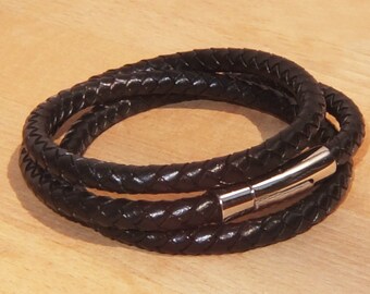 Puede incluir: Un brazalete de cuero negro con un diseño trenzado y un cierre magnético plateado.