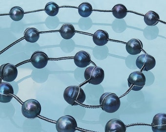 Può includere: Una collana di perle blu scuro su un cordoncino nero. Le perle sono rotonde e hanno una leggera lucentezza iridescente.