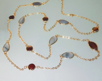 Puede incluir: Un collar de cadena de oro con piedras ovaladas y redondas alternas. Las piedras ovaladas son de color gris claro y las piedras redondas son de color rojo oscuro.