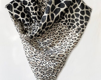 May include: A sheer scarf with a black and beige animal print pattern. The scarf is folded and draped, showcasing the varying sizes of the spots. The scarf is made of a lightweight material.