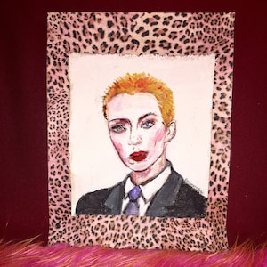 May include: A painting of a person with short, blonde hair wearing a black suit and a purple tie. The painting is framed with a leopard print border.