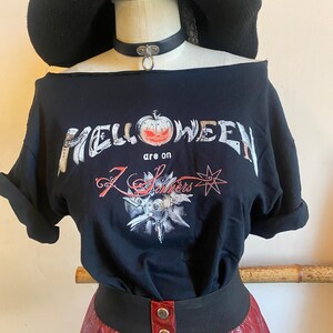 May include: Black t-shirt with a graphic print of the band "Helloween" with the text "are on 7 Sinners" and a pumpkin graphic. The shirt has a slightly off-the-shoulder style.