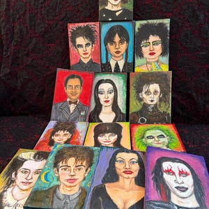 May include: A collection of small, rectangular paintings featuring portraits of characters from gothic and horror films. The paintings showcase a variety of styles and colors, with subjects including The Crow, Wednesday Addams, and Beetlejuice.