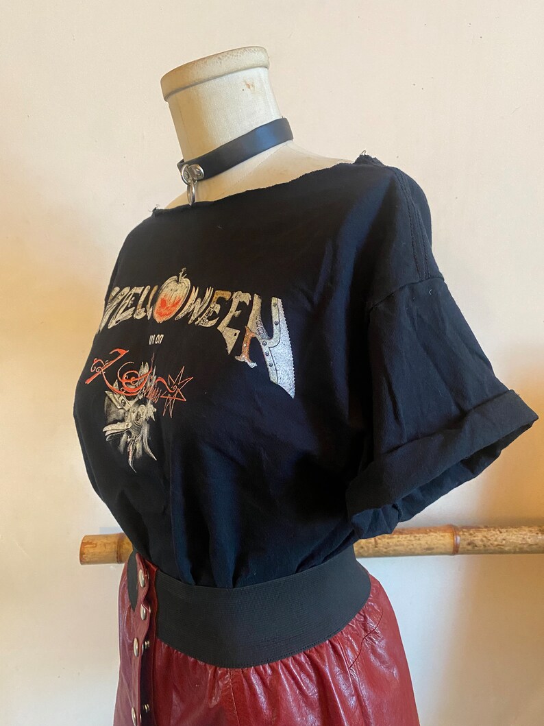 May include: Black t-shirt with a graphic print of the word "Halloween" with an apple and a skull design. The shirt has a distressed look and is worn with a black leather choker and a red leather skirt.