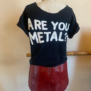 May include: Black t-shirt with white text that reads "Are You Metal?" on the back. The t-shirt is paired with a burgundy leather skirt.