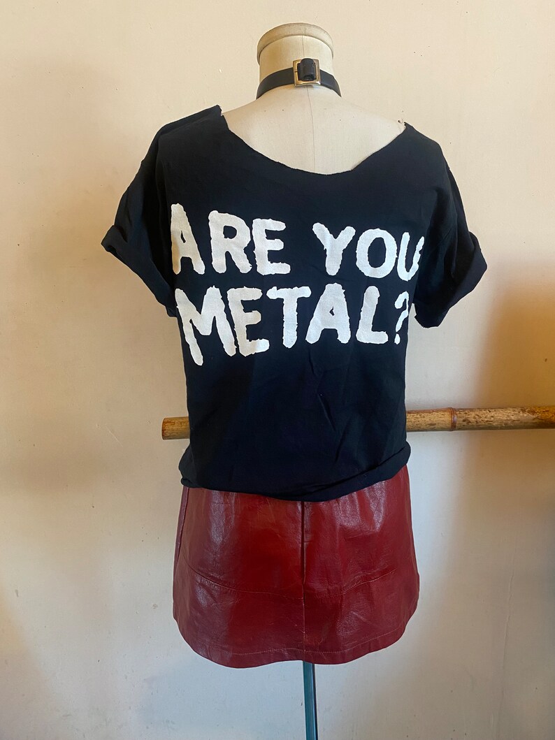 May include: Black t-shirt with white text that reads "Are You Metal?" on the back. The t-shirt is paired with a burgundy leather skirt.