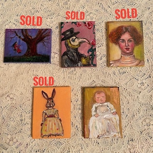 May include: Five small paintings on canvas, each with a different subject. The paintings are all framed in simple wooden frames. The subjects of the paintings are a girl swinging from a tree, a plague doctor, a woman with red hair, a rabbit wearing a dress, and a baby.