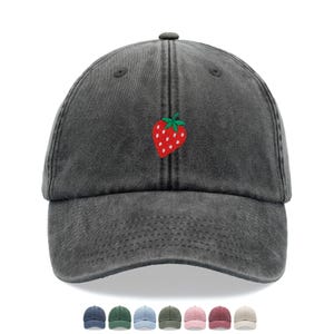 Puede incluir: Gorra de béisbol gris carbón con visera curva y correa ajustable. La gorra presenta una fresa roja bordada con semillas blancas y hojas verdes. La imagen también muestra una fila de gorras de diferentes colores.