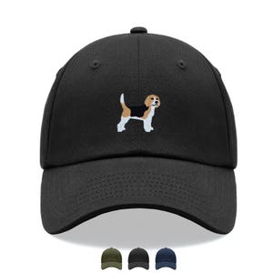 Peut inclure: Une casquette de baseball noire avec un beagle brodé sur le panneau avant. Le chien est représenté avec du fil blanc, beige et noir. Sous la casquette principale, trois versions plus petites sont présentées en vert olive, noir et bleu marine.