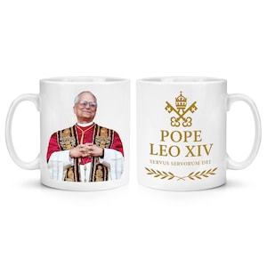 May include: White ceramic mug featuring an image of Pope Leo XIV on one side and the text "POPE LEO XIV SERVUS SERVORUM DEI" with a gold emblem on the other. The mug has a standard handle and a glossy finish.